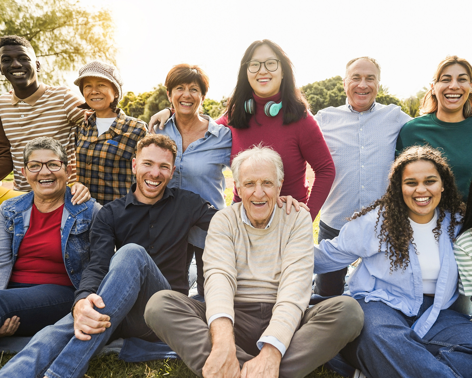 group of racially and age diverse people smiling, sitting outside at a park