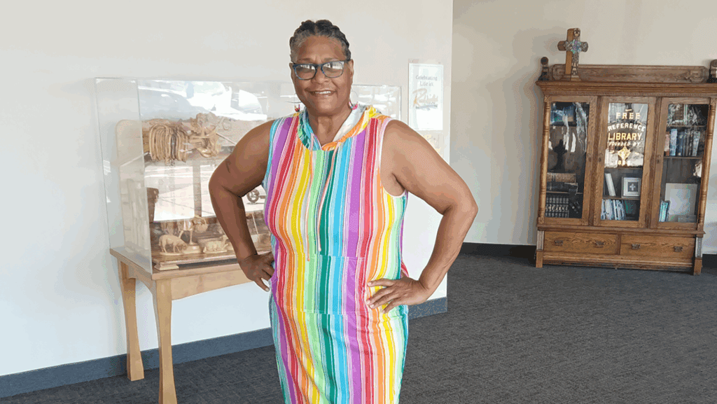 Rosa smiling in dress with brightly colored stripes posed with her hands on her hips