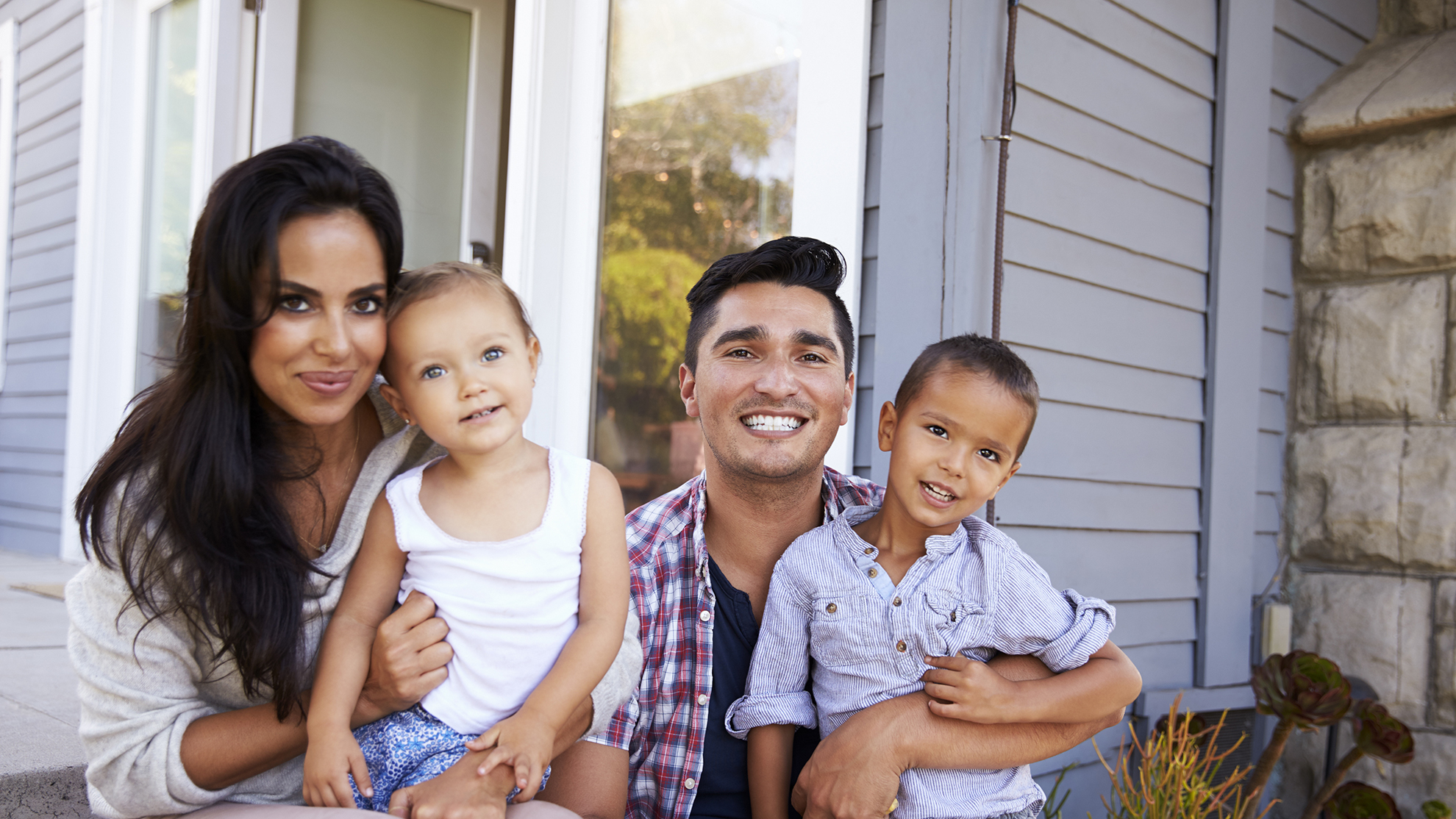 mother, father, and 2 children smiling while sitting on the stoop in front of their home