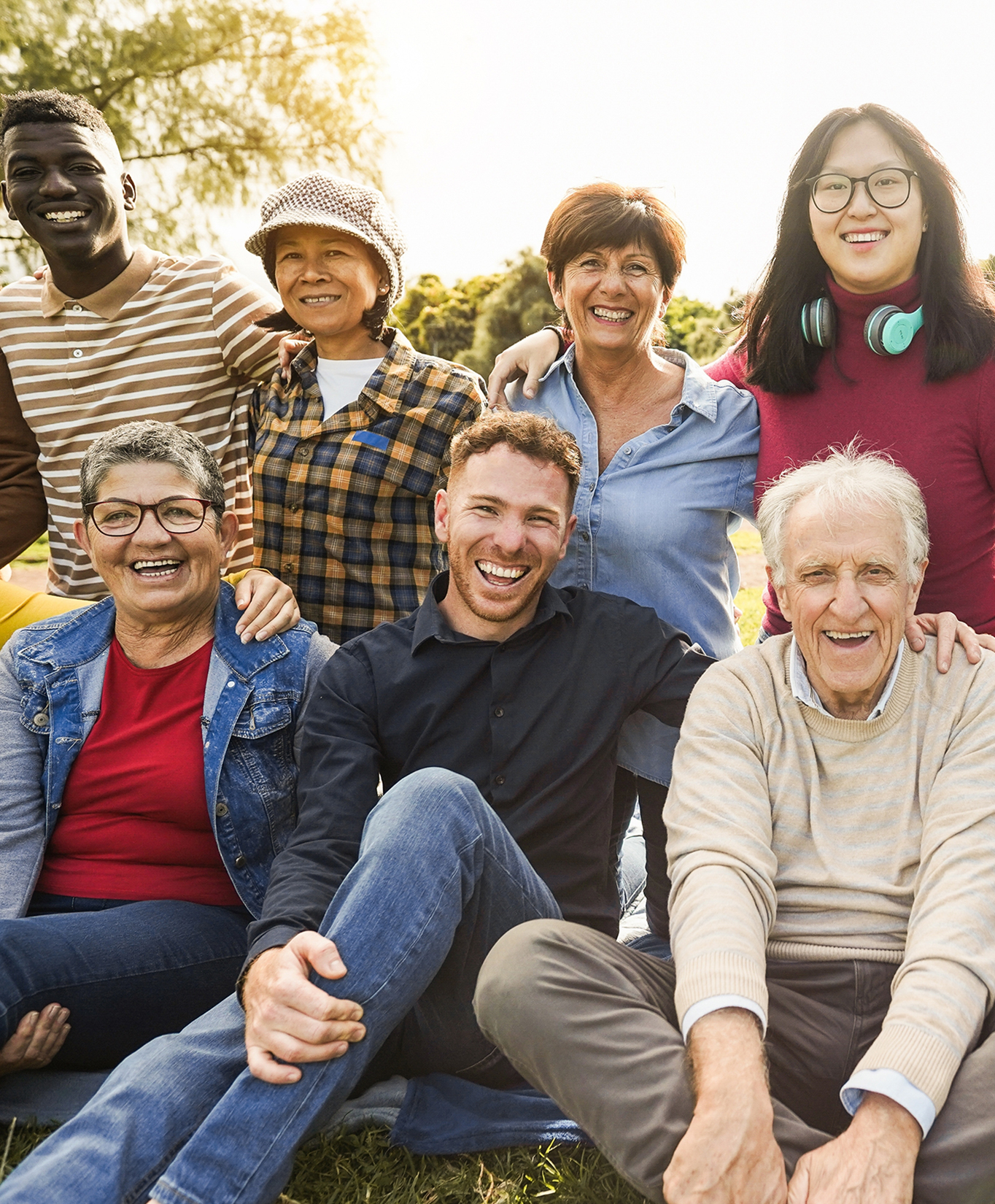 group of racially and age diverse people smiling sitting outside at a park