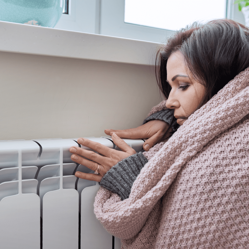 woman wrapped in a blanket warming her hands at a heater
